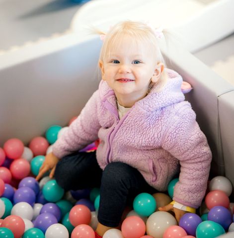 A little girl is sitting in a ball pit filled with colorful balls at The Lemon Lounge Indoor Playground