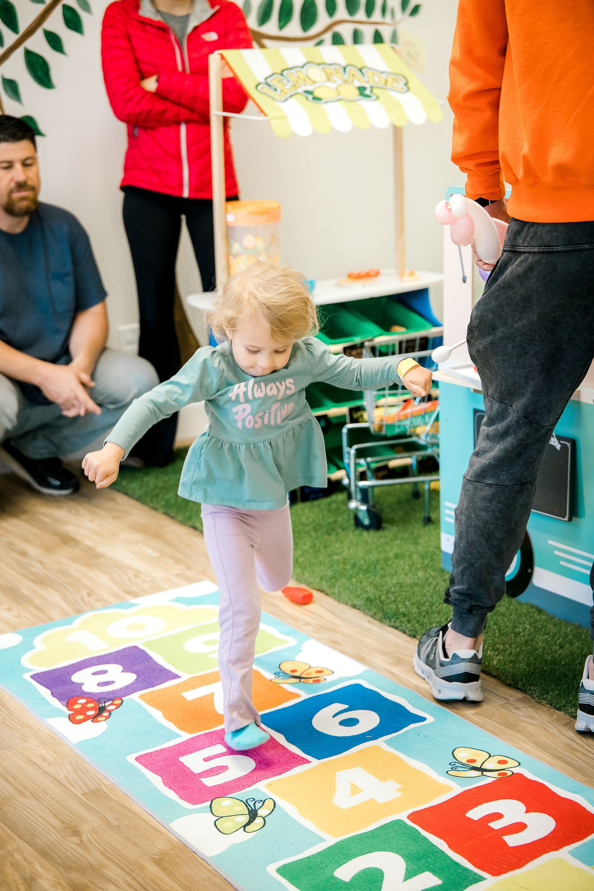 A little girl is playing hopscotch on a rug at The Lemon Lounge Indoor Playground.