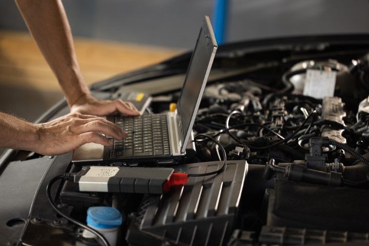 Person using a laptop on a car engine while the hood is open