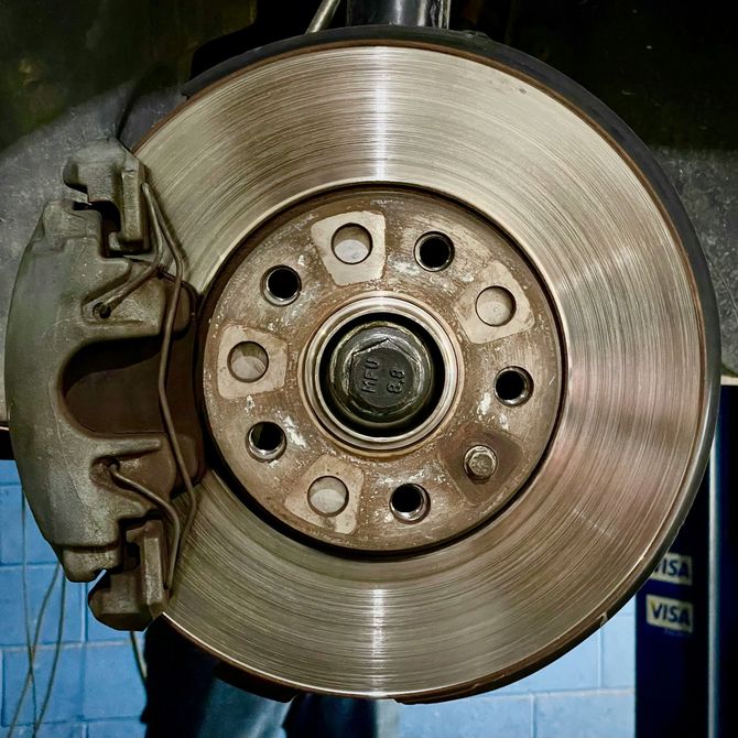 Car wheel brake disc and caliper close-up, showing wear grooves on the rotor.