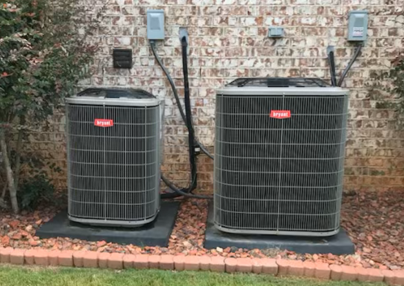 Two air conditioners are sitting next to each other in front of a brick wall.