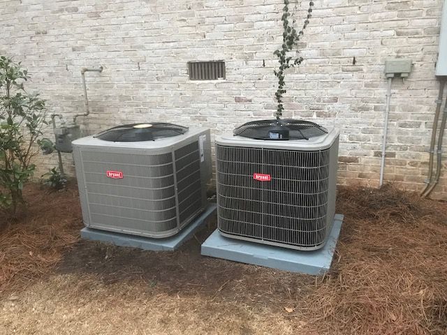 Two air conditioners are sitting next to each other in front of a brick wall.