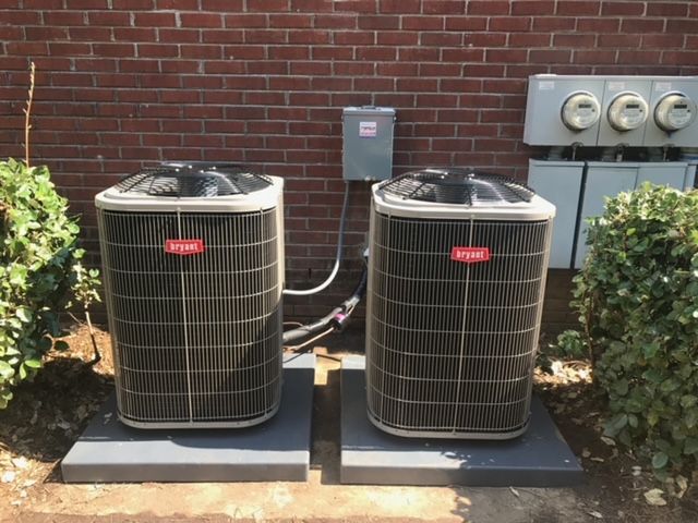 Two air conditioners are sitting next to each other in front of a brick building.