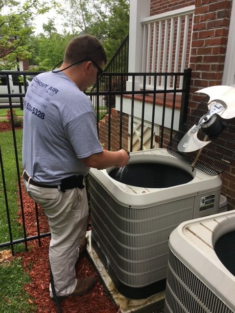 A man is working on an air conditioner outside of a house