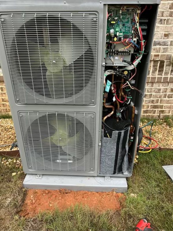 A large air conditioner is sitting on the ground in front of a brick building.