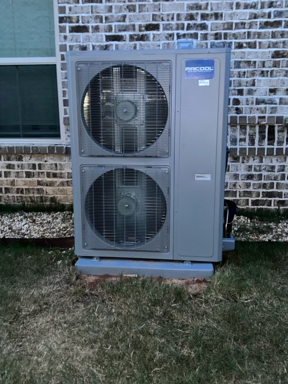 A large air conditioner is sitting in front of a brick building.