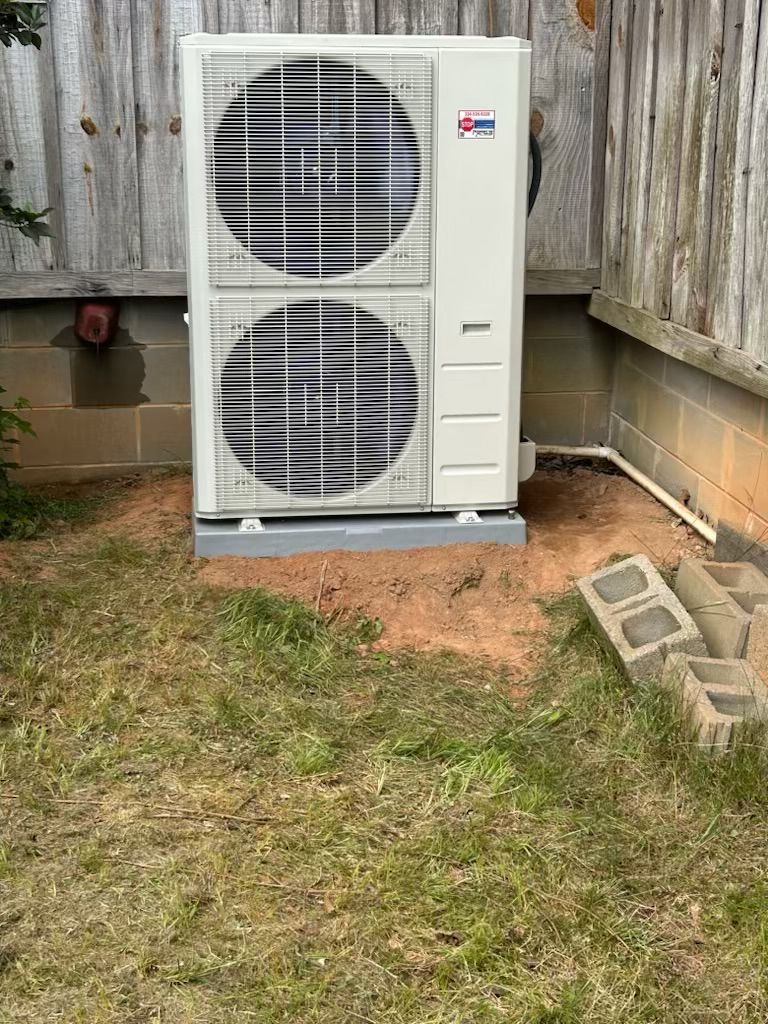 A large air conditioner is sitting in the grass next to a fence.