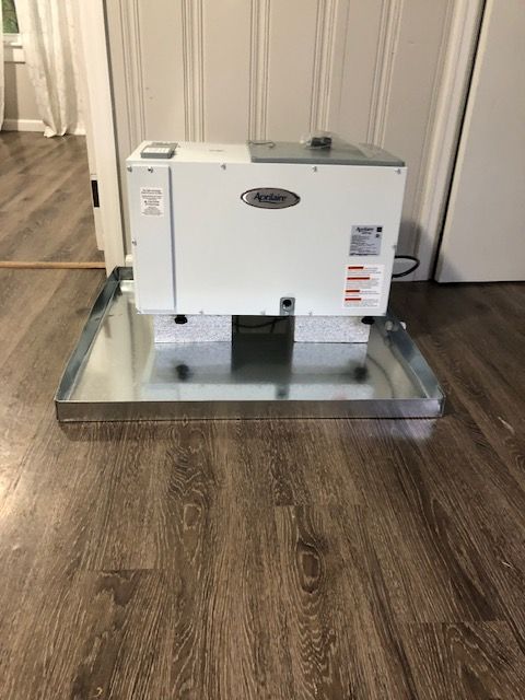 A white machine is sitting on top of a metal tray on a wooden floor.