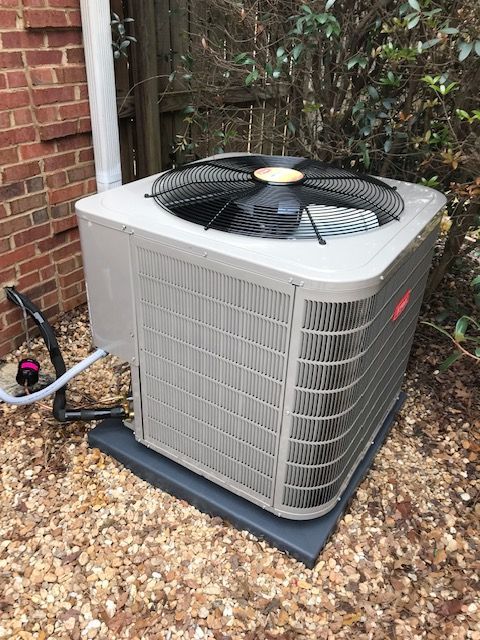 A large air conditioner is sitting on top of a pile of gravel next to a brick wall.