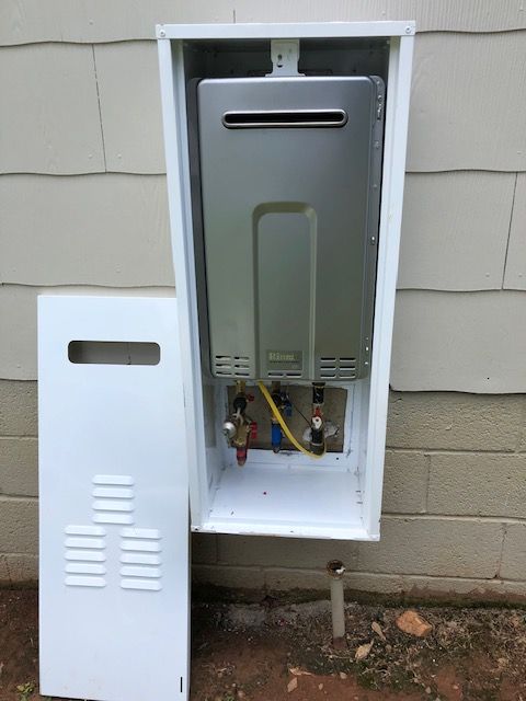 A water heater is sitting inside of a white box on the side of a building.