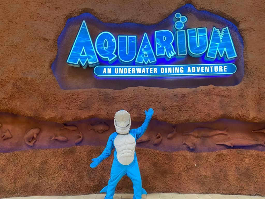 Person in a blue shark costume waving in front of an 