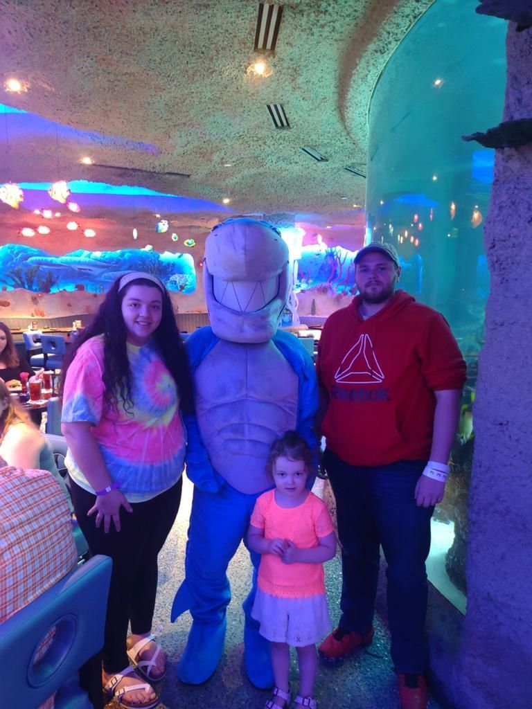 Family poses with a blue shark mascot in a restaurant with aquatic decor.