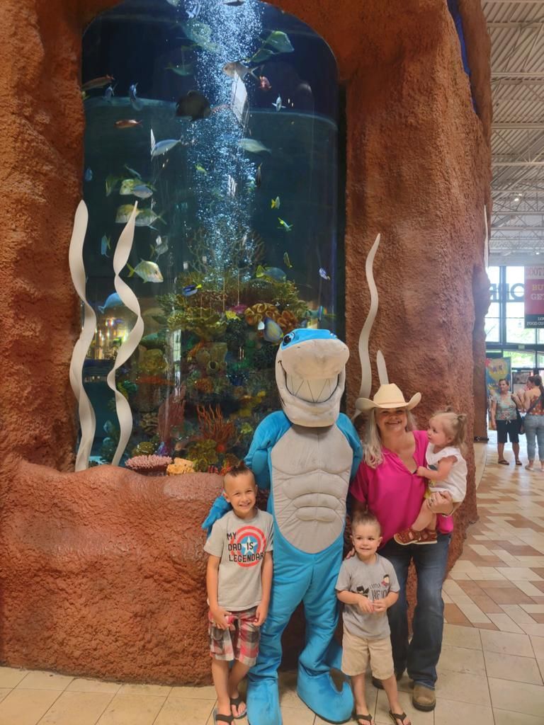 Family posing with a mascot and a large aquarium filled with fish. Brown rock structure.