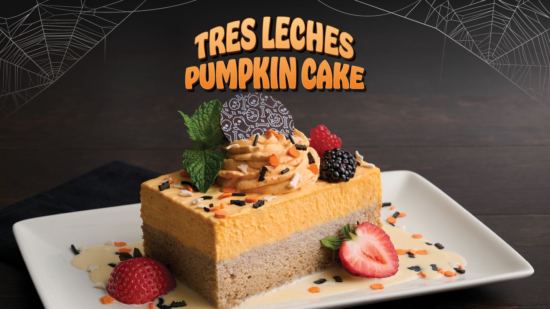 Tres Leches pumpkin cake with orange frosting, garnished with berries and chocolate, on a white plate.