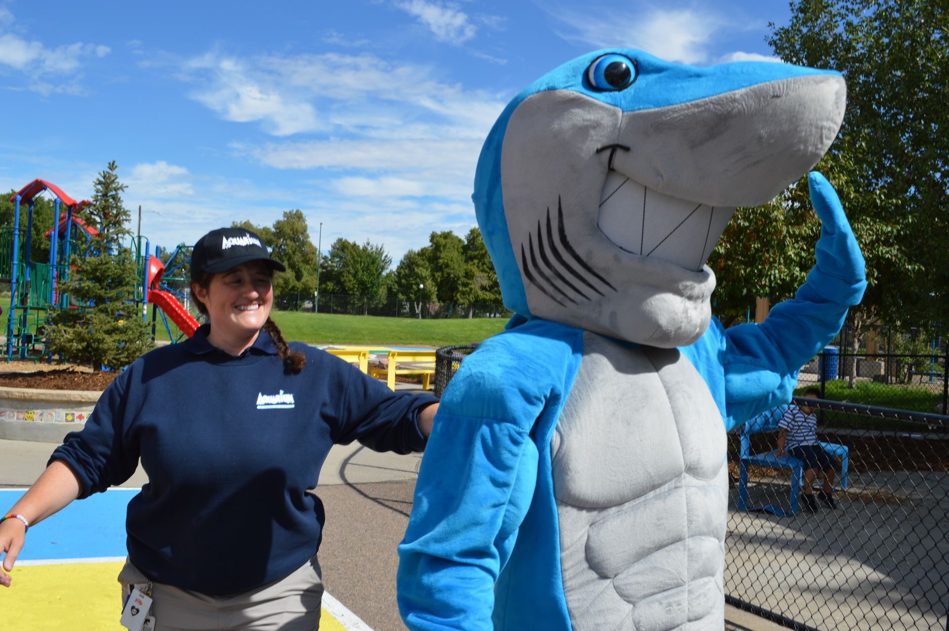 A woman standing next to a blue and white shark mascot