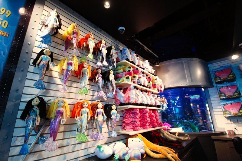 Mermaid dolls and stuffed animals for sale on a store wall, with an aquarium in the background.