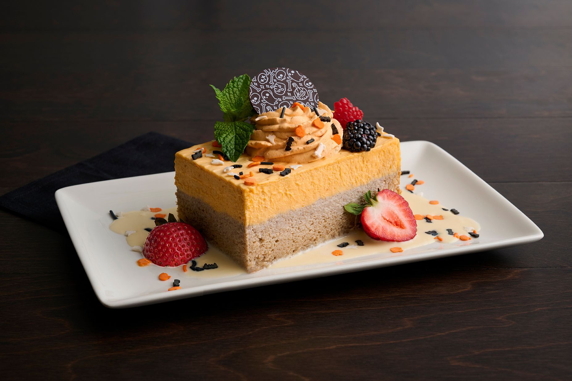 Pumpkin spice cake slice with whipped cream, berries, and sprinkles on a white plate.