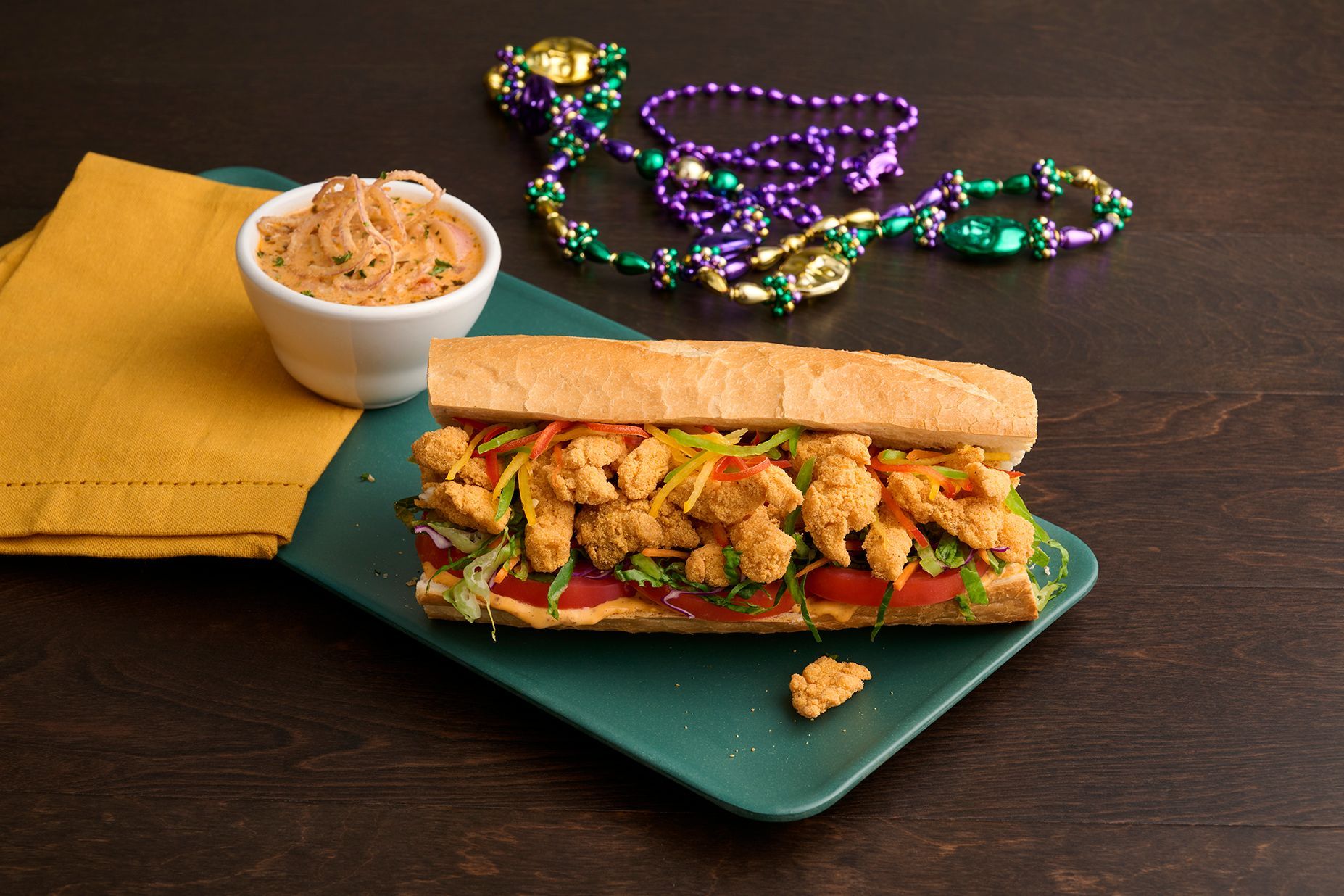 Po'boy sandwich with fried food and Mardi Gras beads on a green plate.