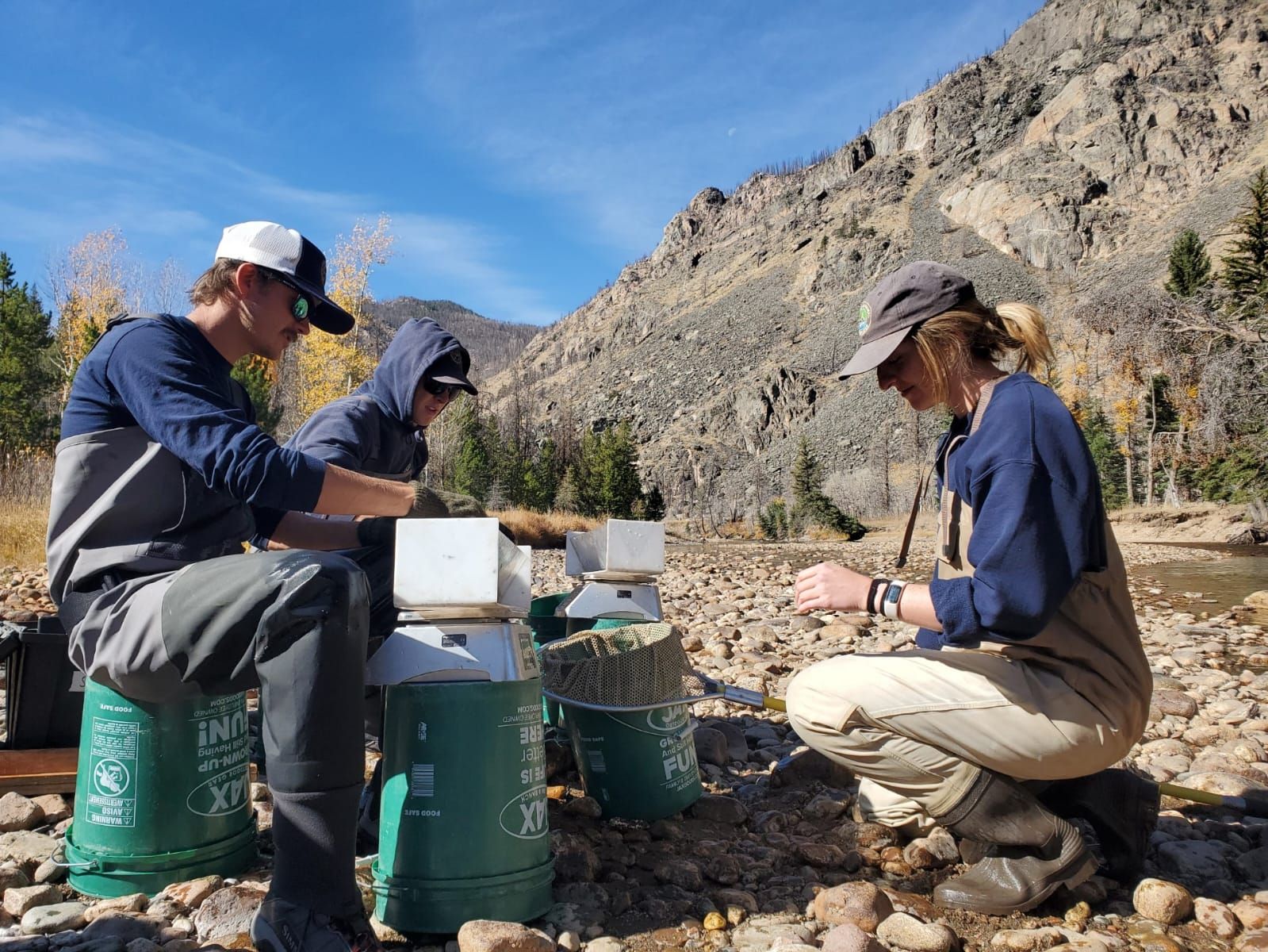 A group of people are sitting on green buckets near a river