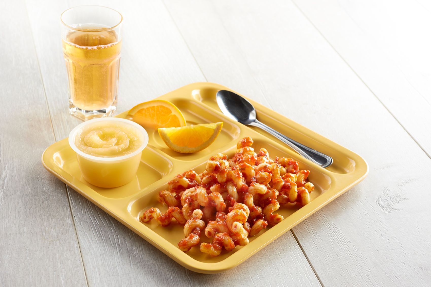 A yellow cafeteria tray with macaroni, applesauce, orange slices, a drink, and a spoon.