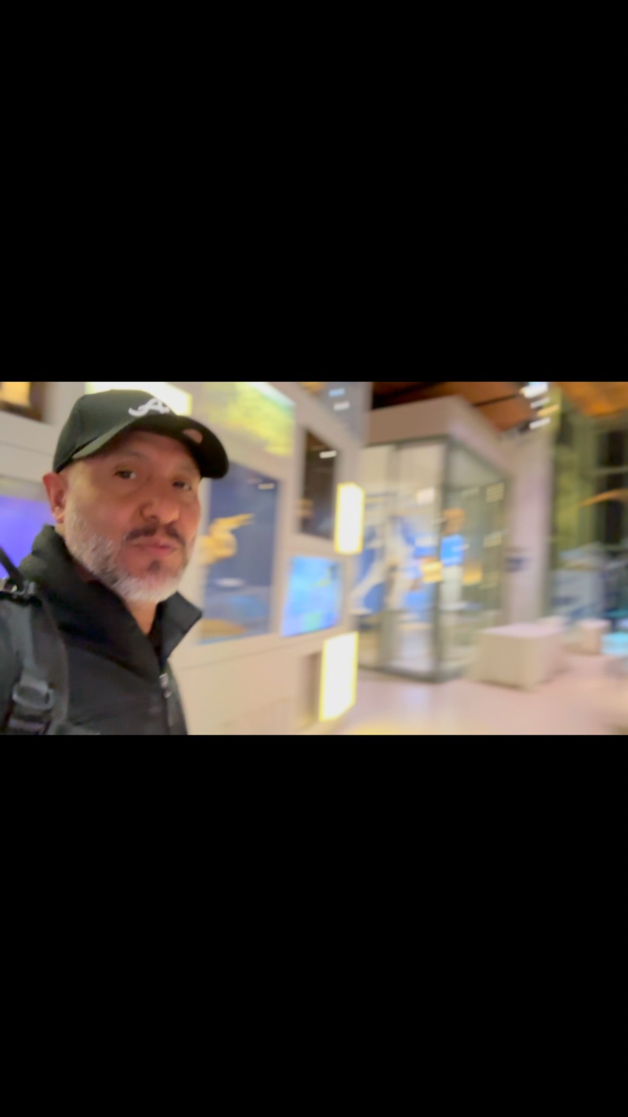 Man in a green cap taking a selfie outside a storefront at night
