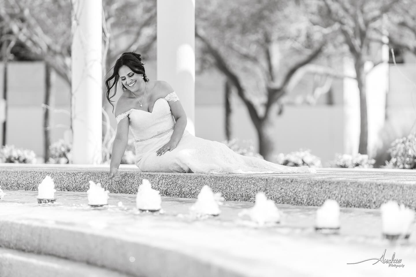 Woman in a white dress sitting by a fountain in a black-and-white outdoor scene
