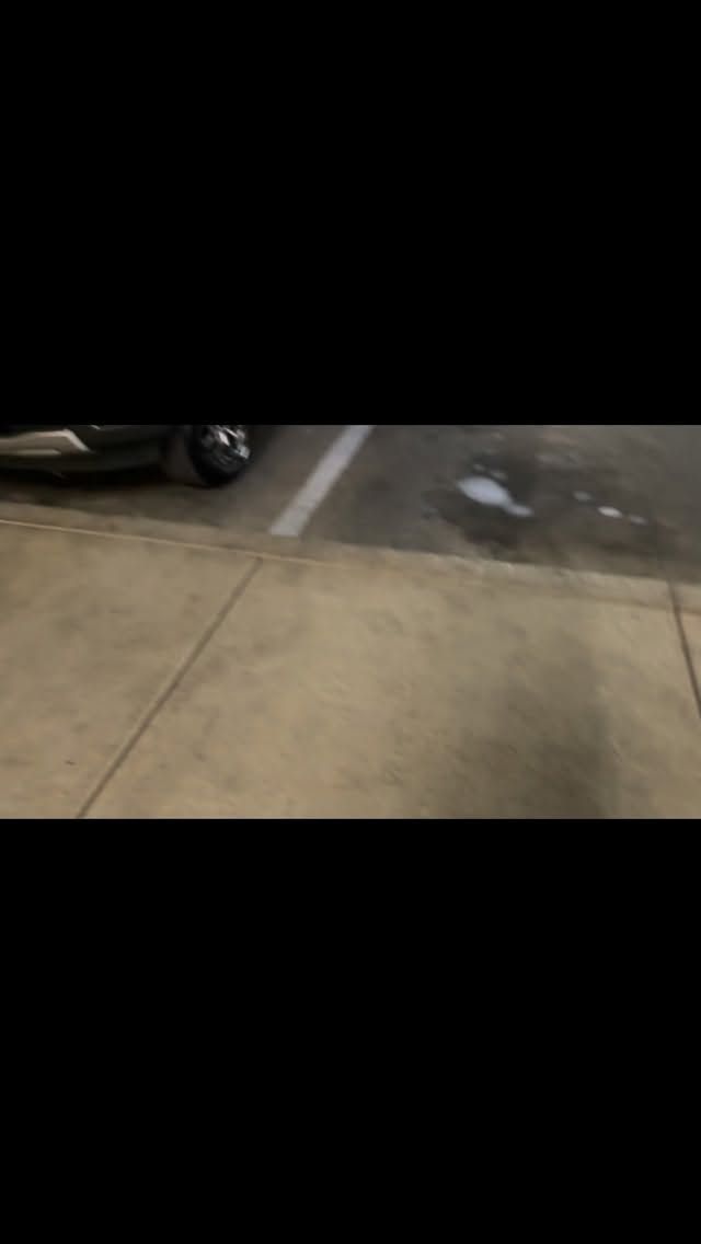 Wet sidewalk beside a parked car, with a small puddle near a painted parking line.