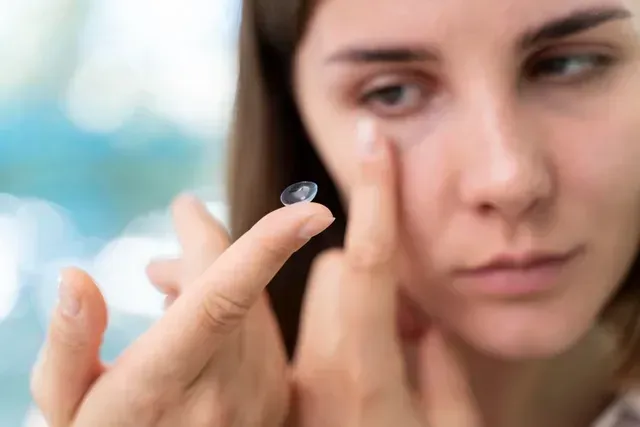 A woman is putting a contact lens in her eye.