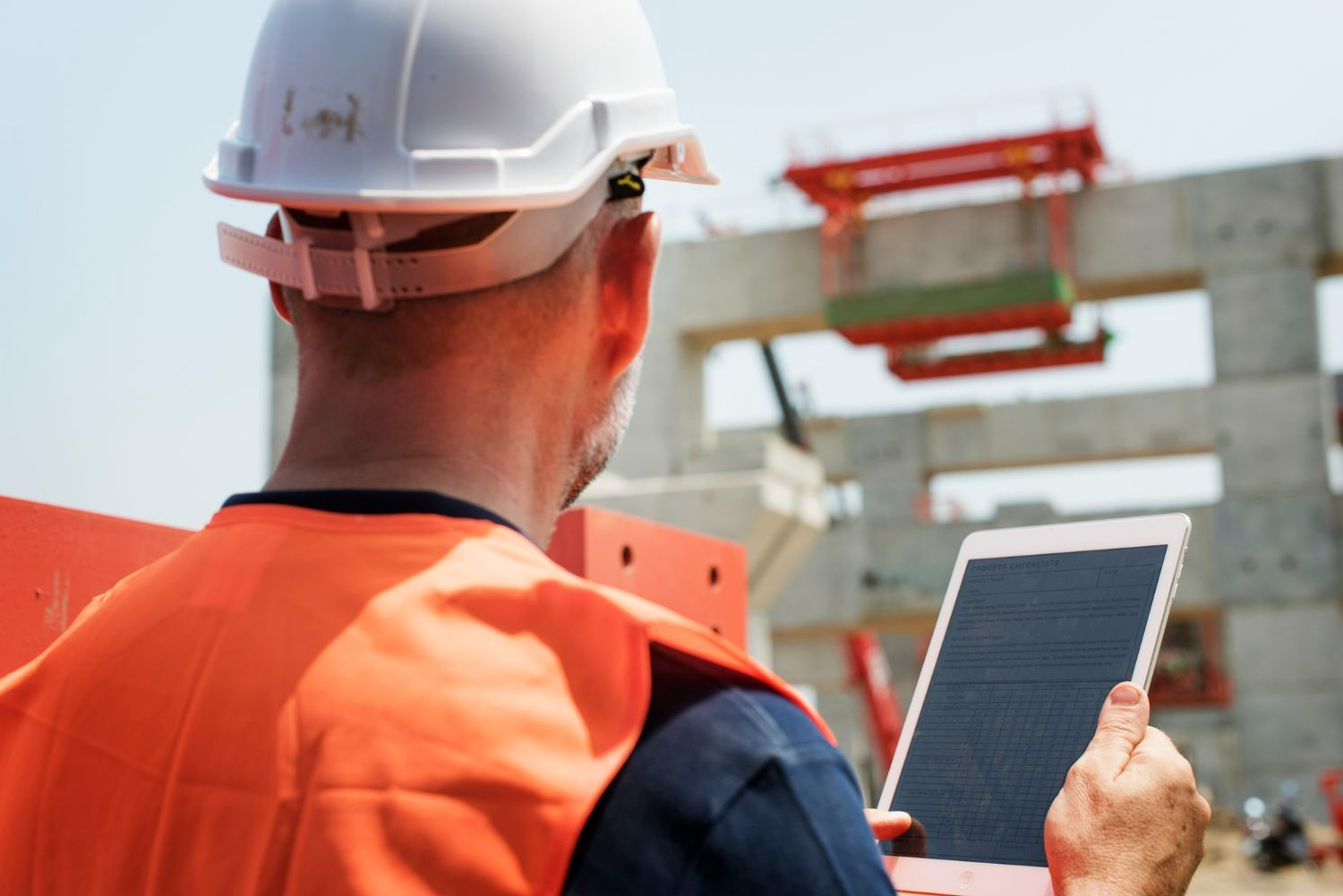 A construction worker is looking at a tablet at a construction site.