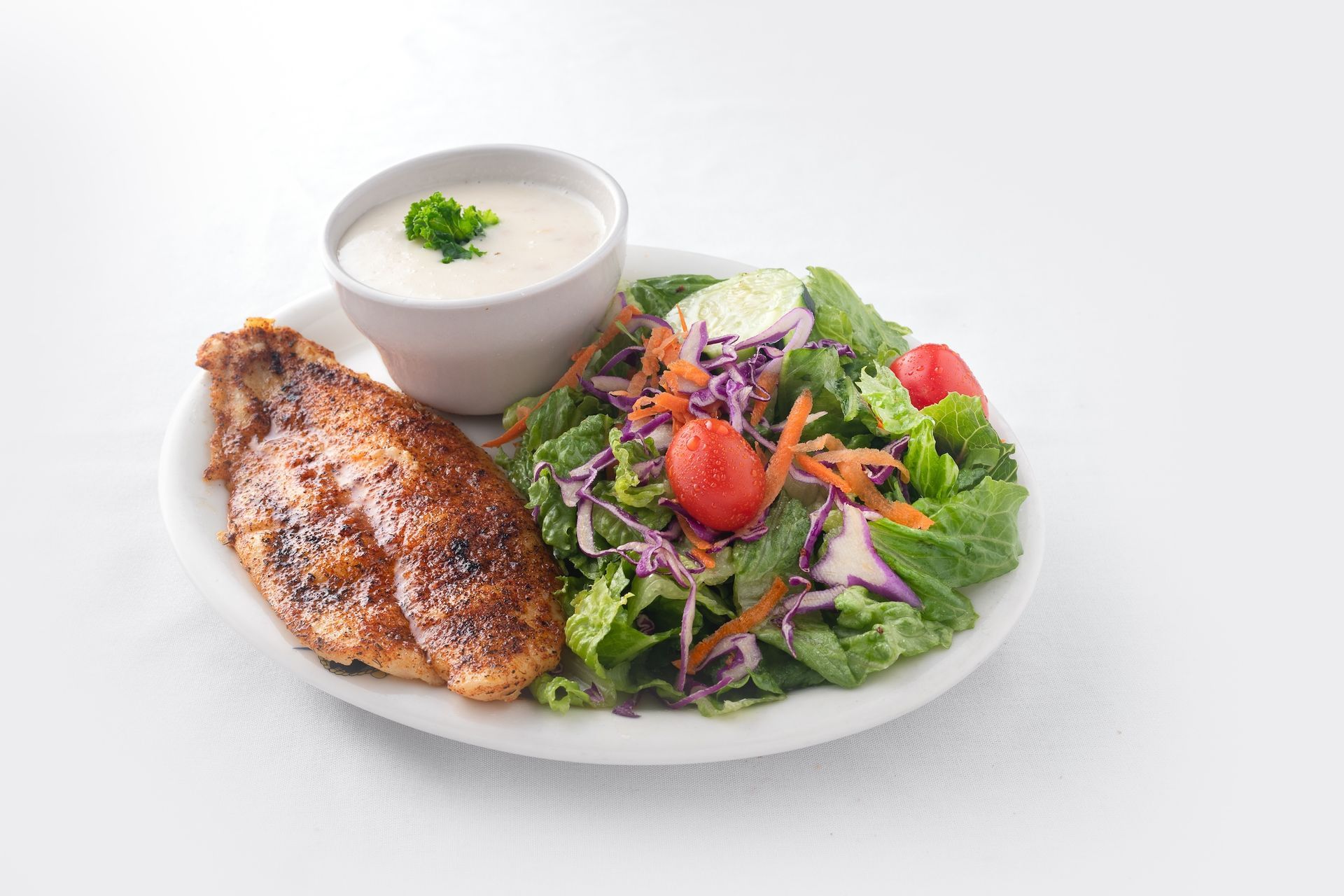 A plate of food with chicken and a salad and a bowl of ranch dressing.