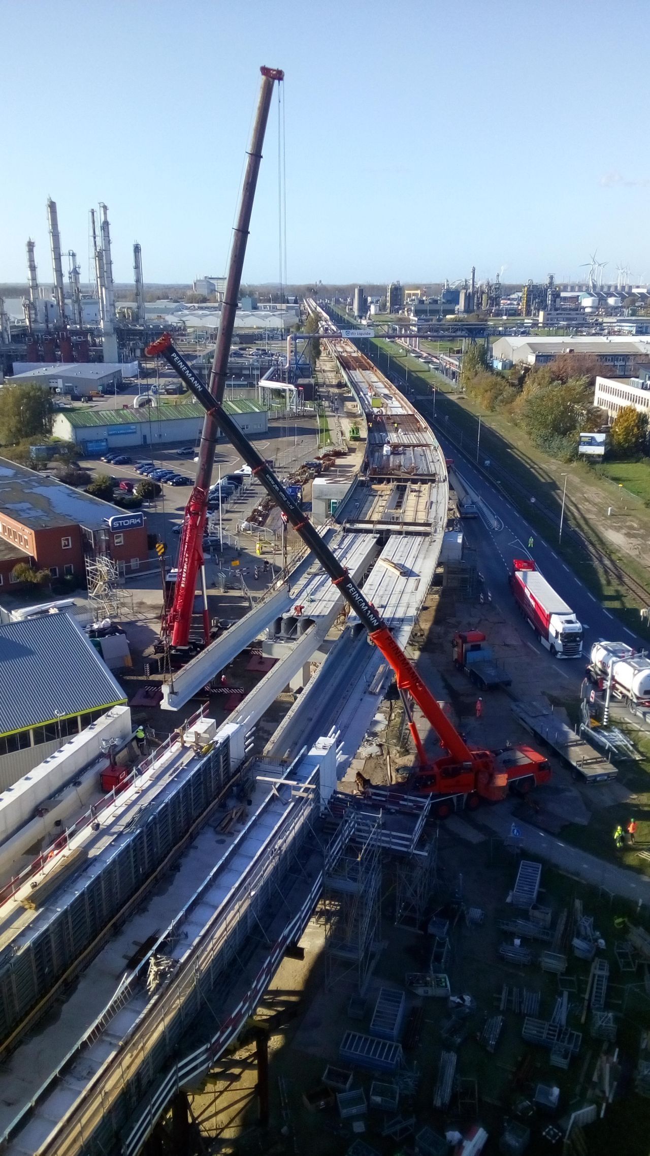 Bouwplaats met twee rode kranen die betonnen balken hijsen.