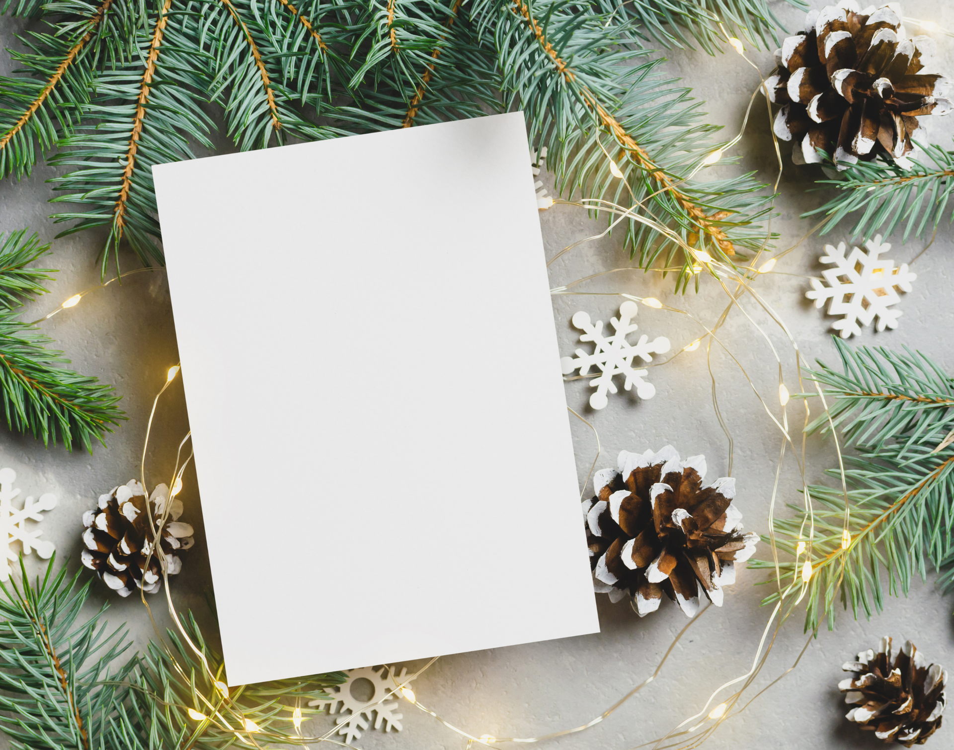 A white card is surrounded by christmas decorations and pine cones.
