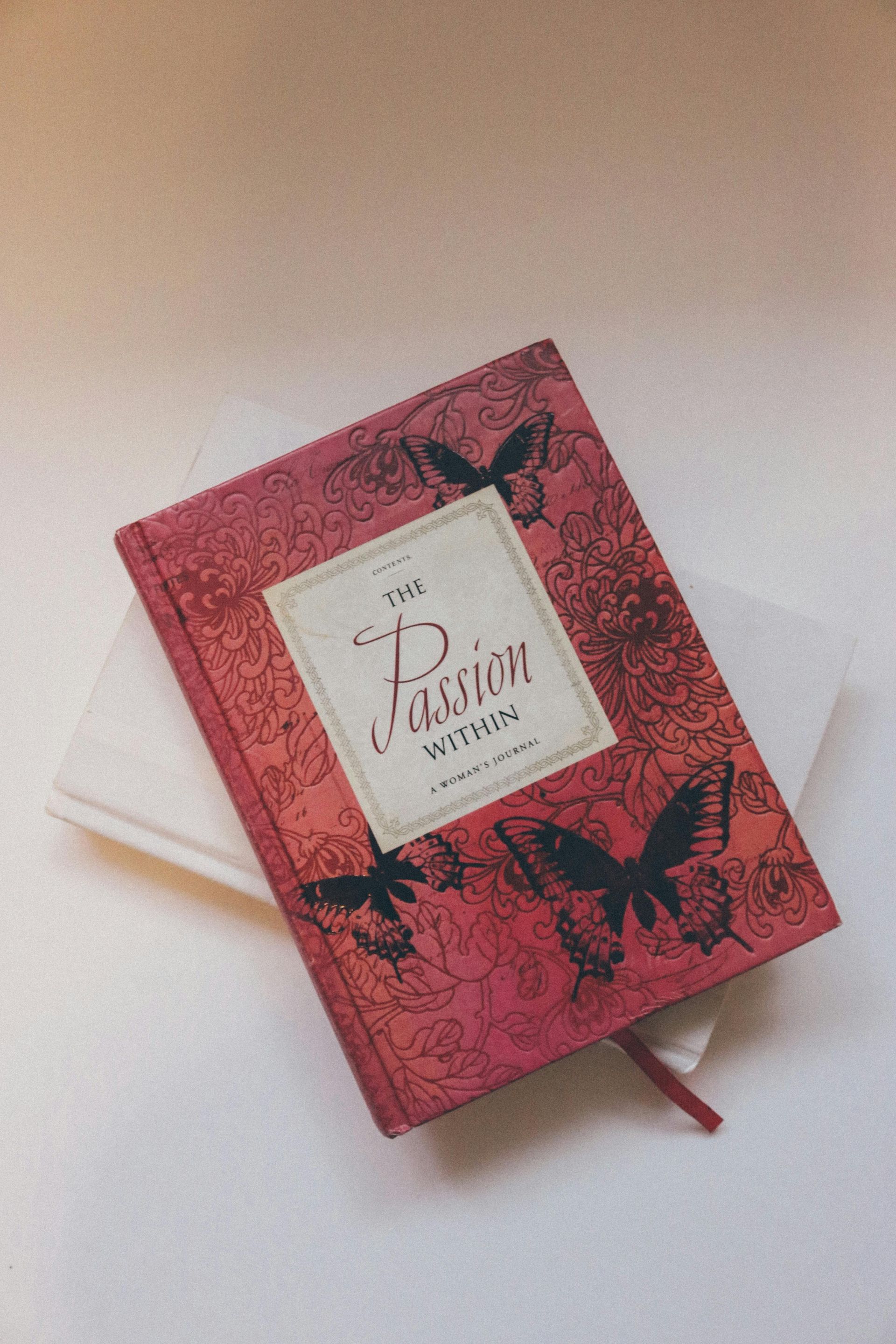 A red book with butterflies on the cover is sitting on top of a white book.