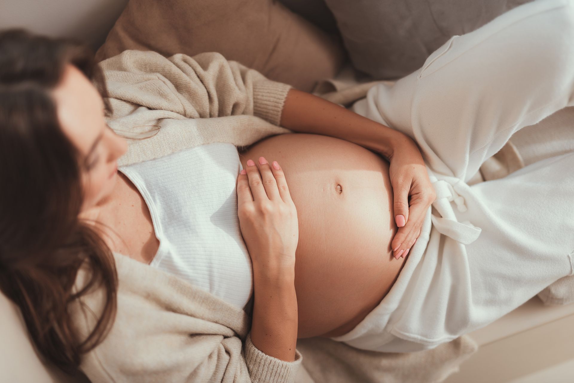 A pregnant woman is laying on a couch holding her belly.
