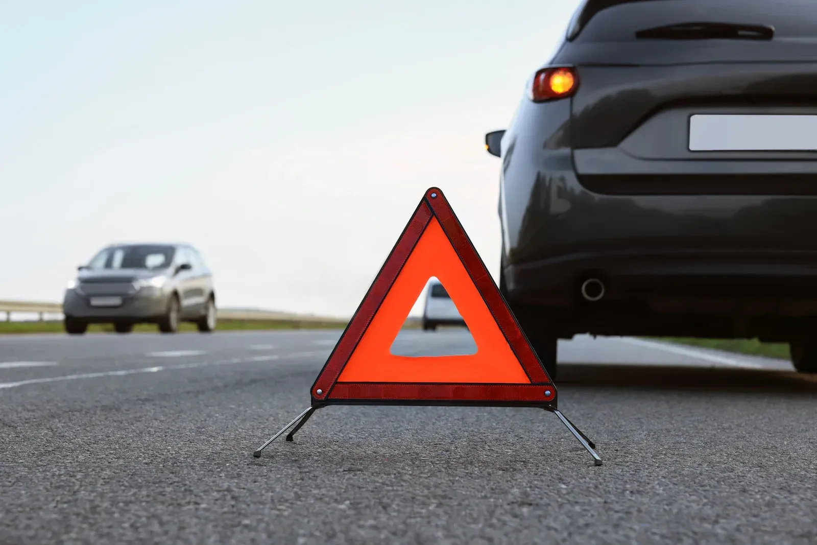 A car is sitting on the side of the road next to a warning triangle.