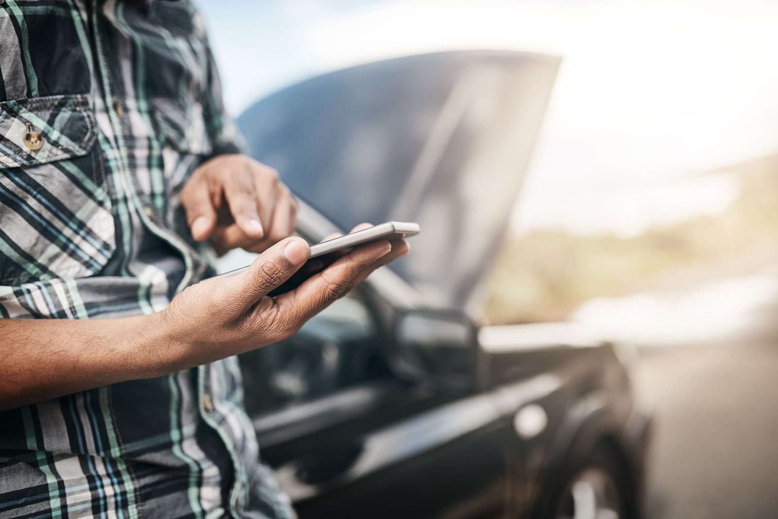 A man is using a cell phone in front of a broken down car.
