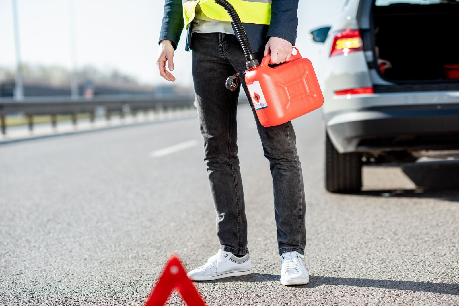 A man is standing on the side of the road holding a gas can.