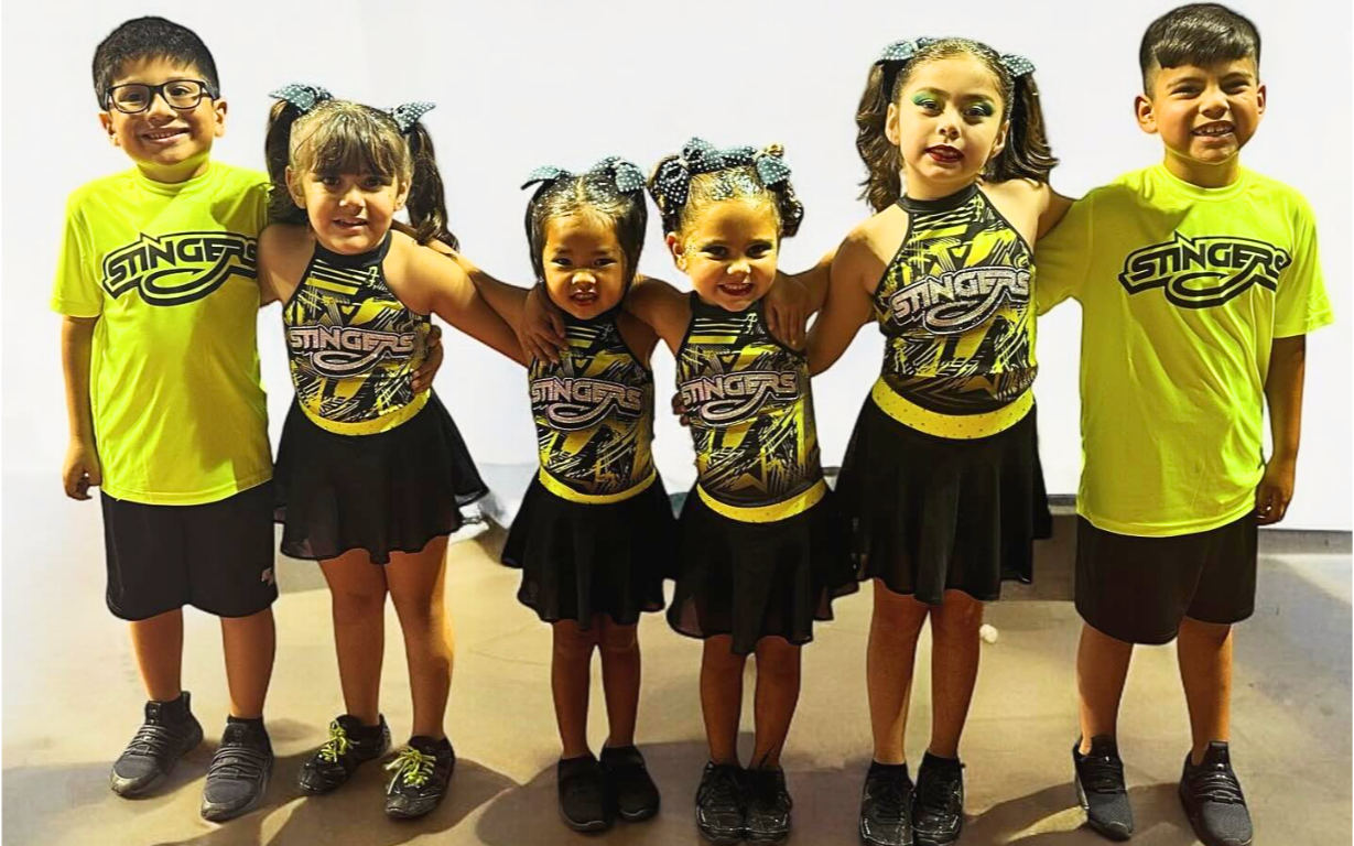 Children in cheerleading uniforms smile with arms around each other.