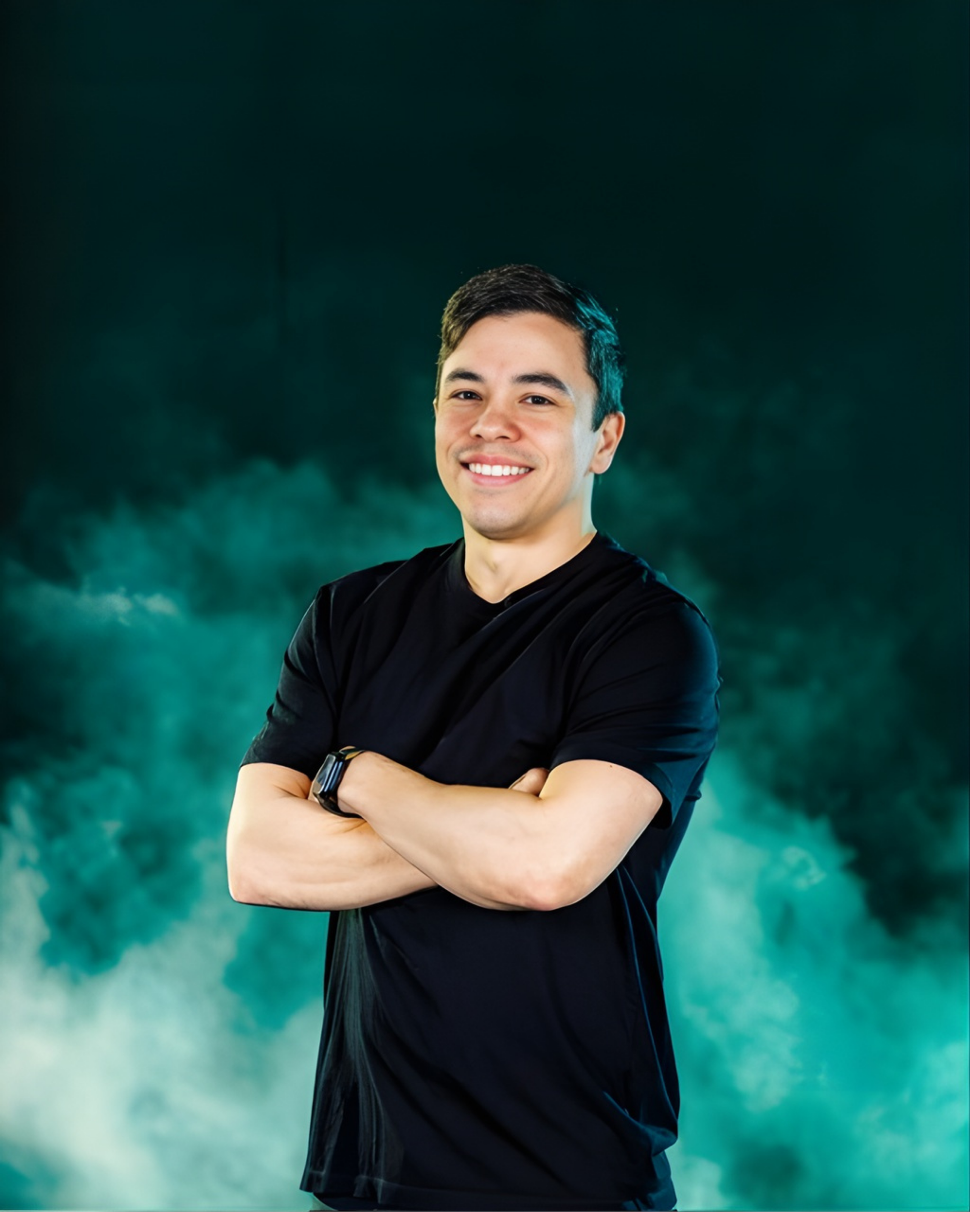 A person in a black t-shirt with arms crossed, smiling against a dark, teal-colored smoky background.