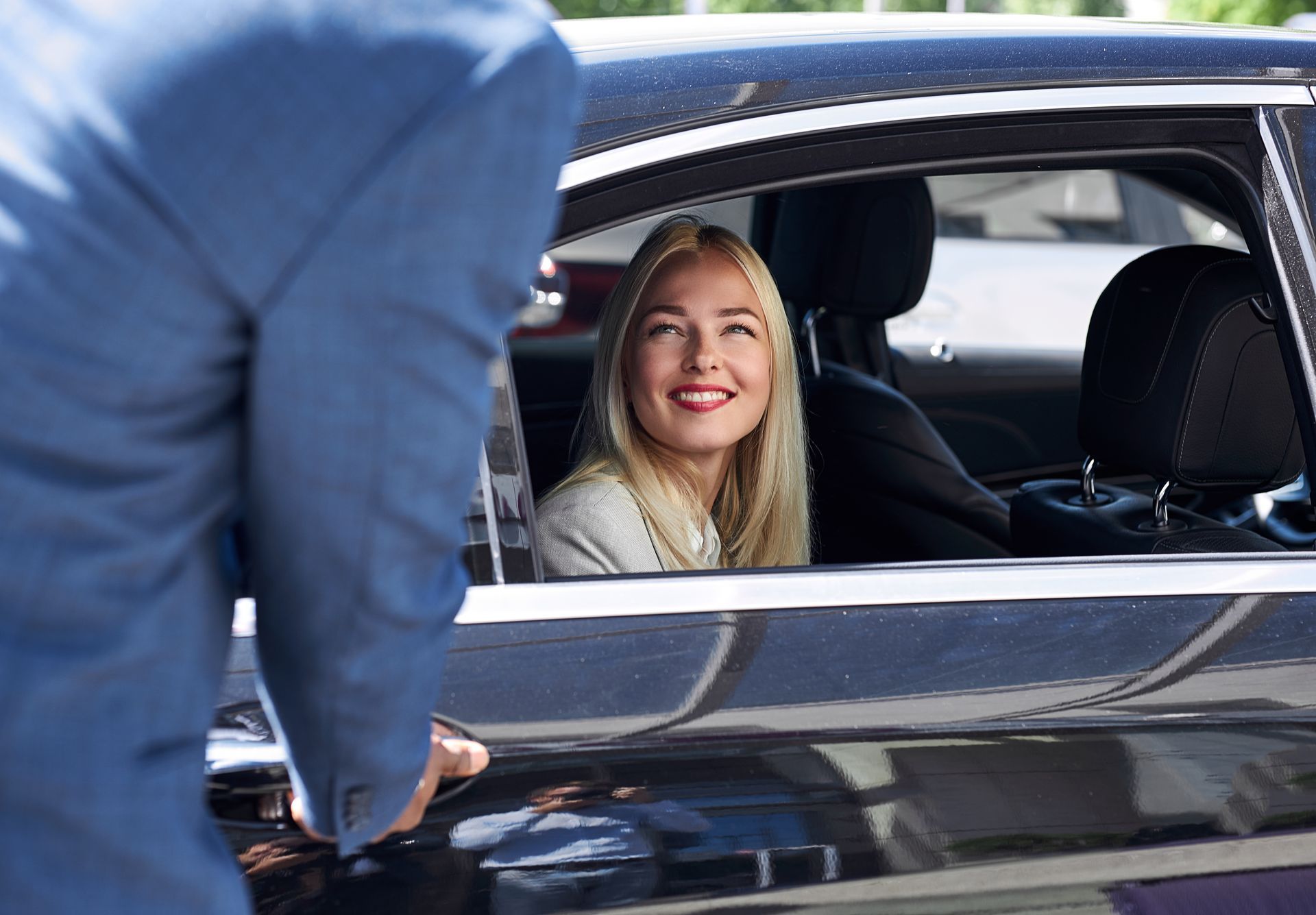 A woman is sitting in a car with a man standing next to her.