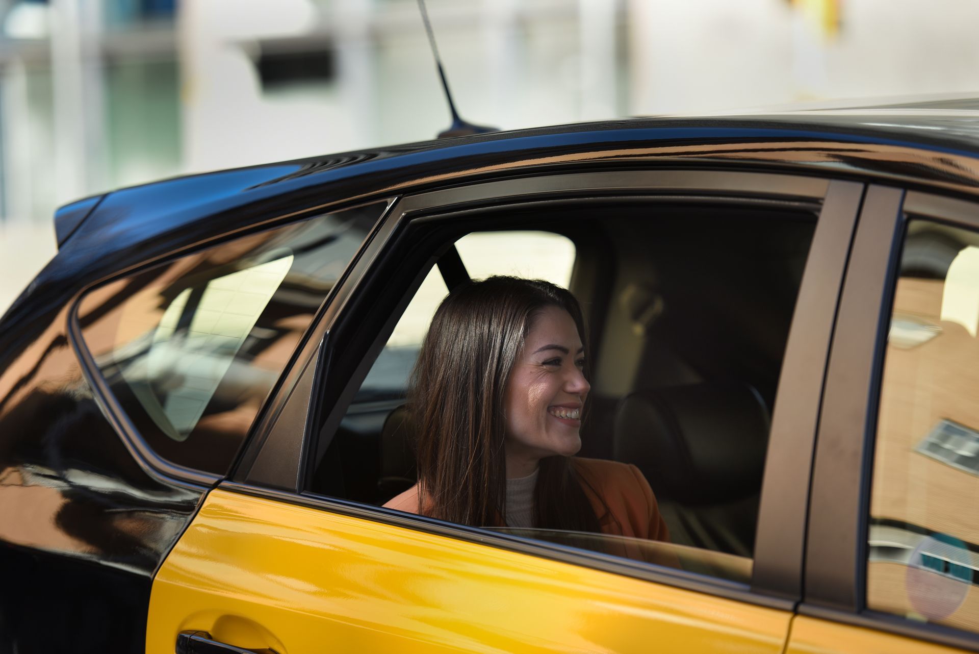 A woman is sitting in a yellow and black car looking out the window.