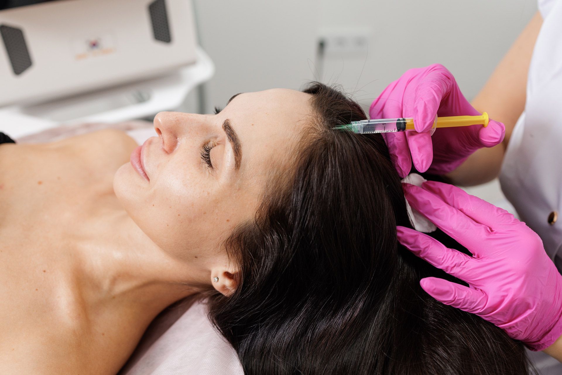 A woman receives an injection on the scalp for hair loss treatment in a clinic.
