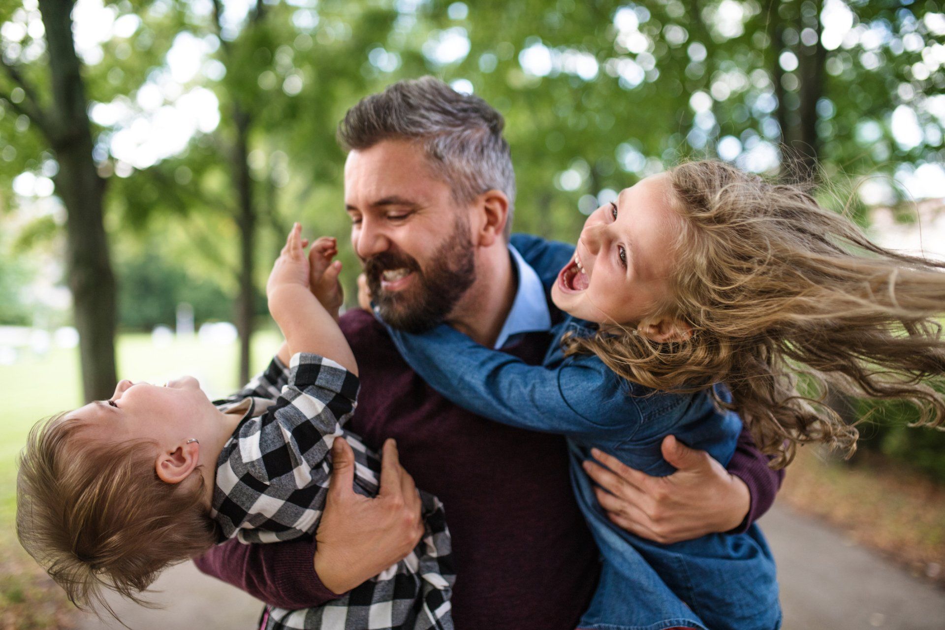Man hugs two children outside; they laugh and play.