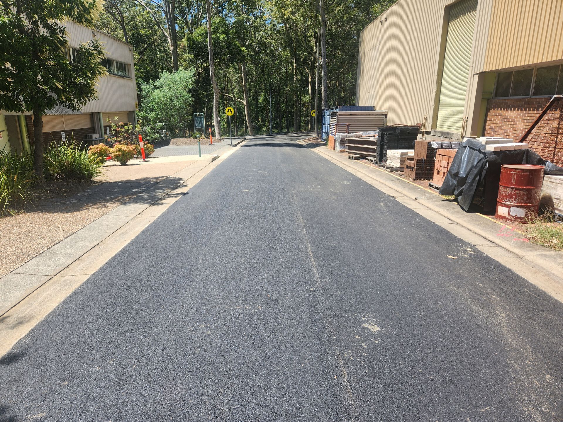 Newly Paved Asphalt Road Between Buildings And Trees — TAC Asphalt Services in Warners Bay, NSW