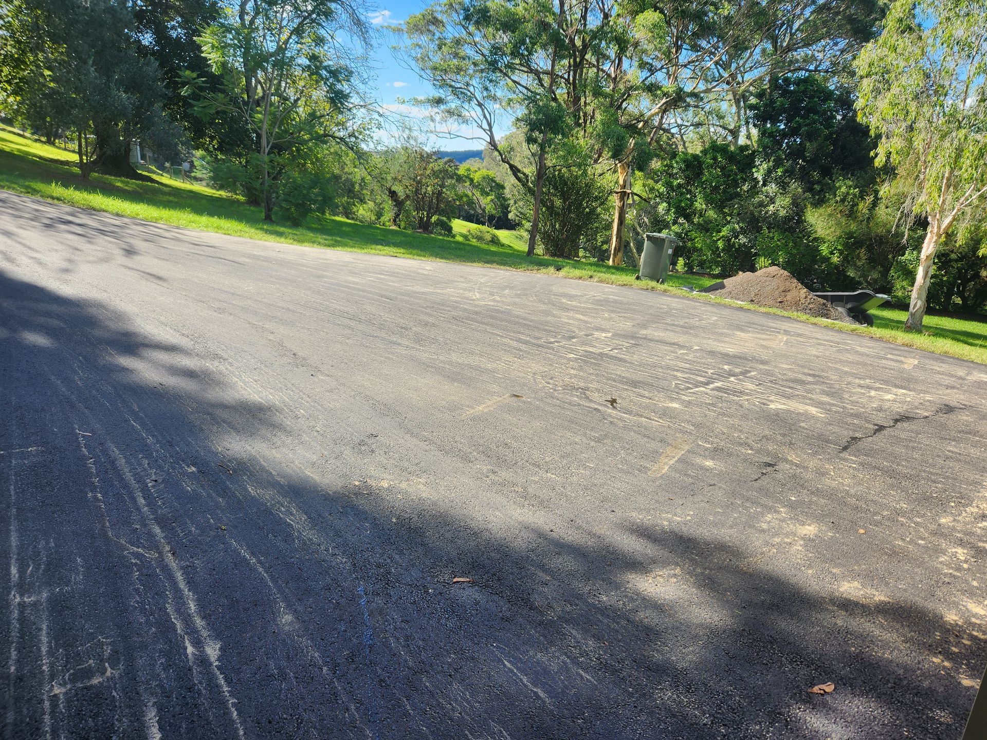 Gravel Driveway On A Grassy Hillside, Trees In The Background Under A Blue Sky — TAC Asphalt Services in Warners Bay, NSW