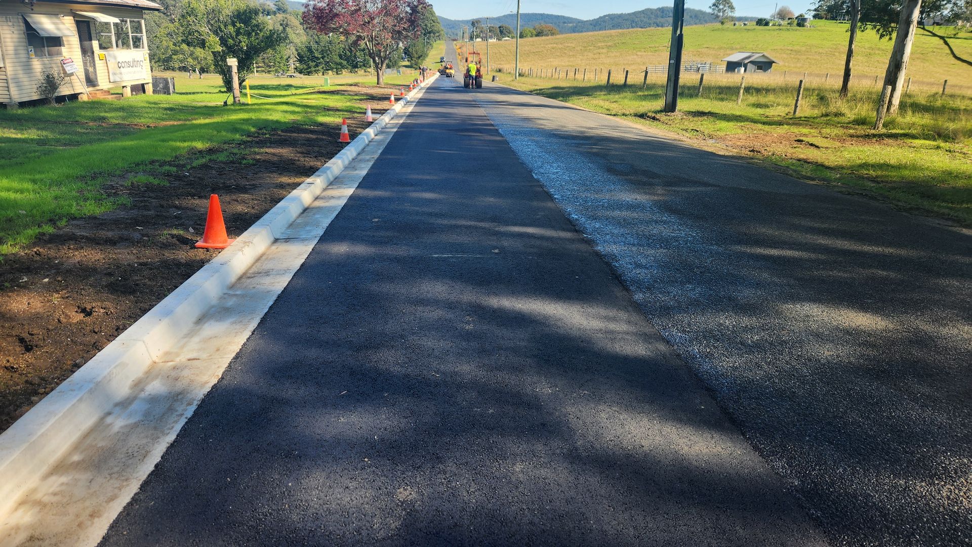 Newly Paved Road With a Concrete Curb, Surrounded by Grass and Trees — TAC Asphalt Services in Warners Bay, NSW