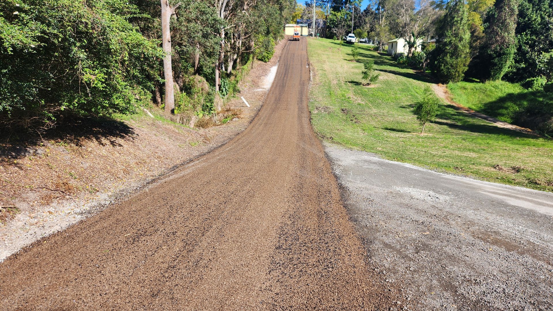 A Gravel Road Slopes Upward Through A Green Landscape — TAC Asphalt Services in Warners Bay, NSW
