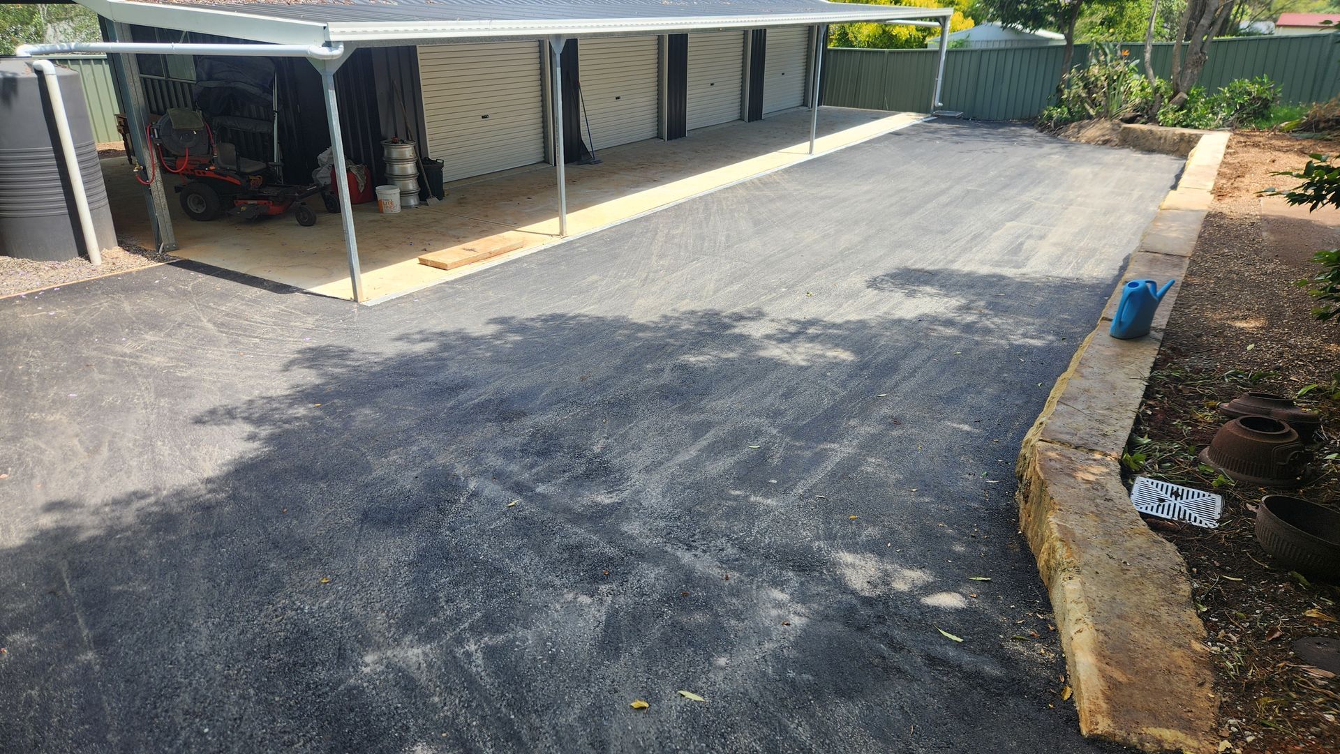 Asphalt Driveway Leading To A Carport With A Lawnmower — TAC Asphalt Services in Warners Bay, NSW