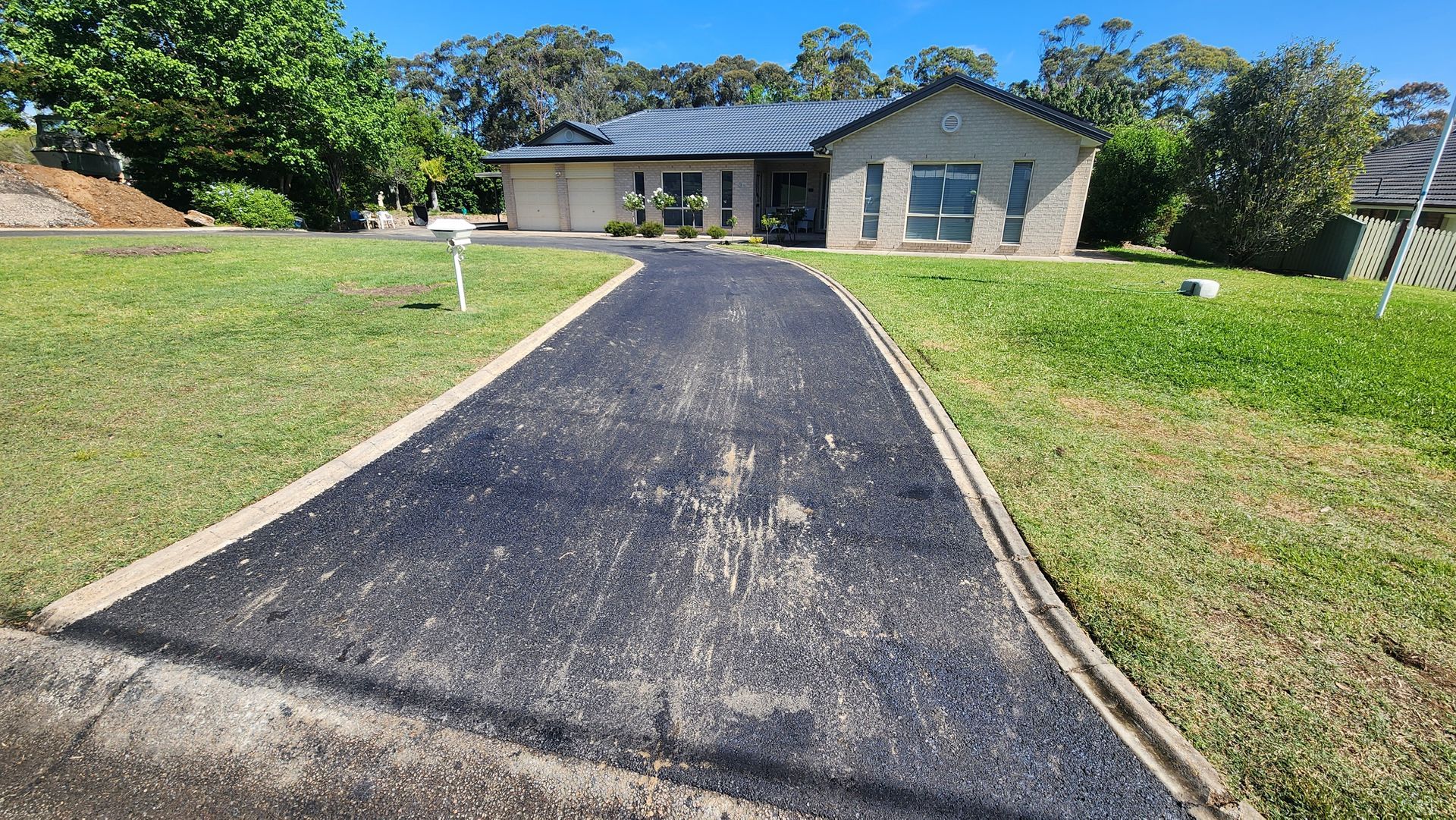 Asphalt Driveway Leads to a Suburban House With a Green Lawn Under a Blue Sky — TAC Asphalt Services in Warners Bay, NSW