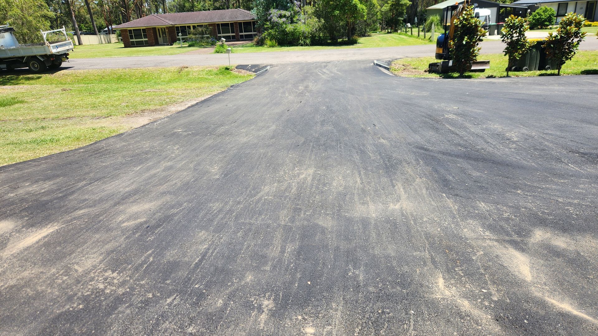 Asphalt Driveway Leading Towards A Grassy Area With Houses And Trees — TAC Asphalt Services in Warners Bay, NSW